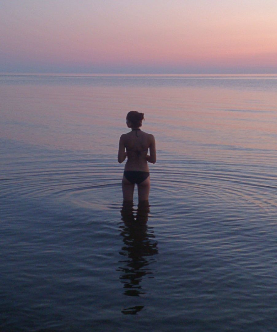 Woman stood in sea at sunset