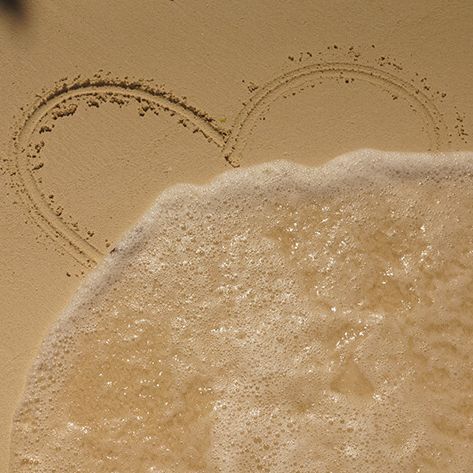 Heart drawn in sand with wave washing over it