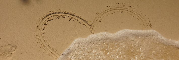 Heart drawn in sand with wave washing over it