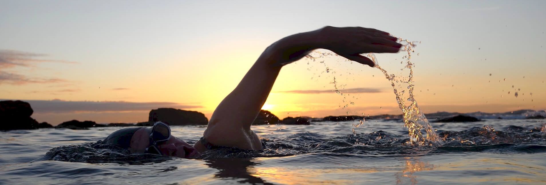 Person swimming in sea at sunset